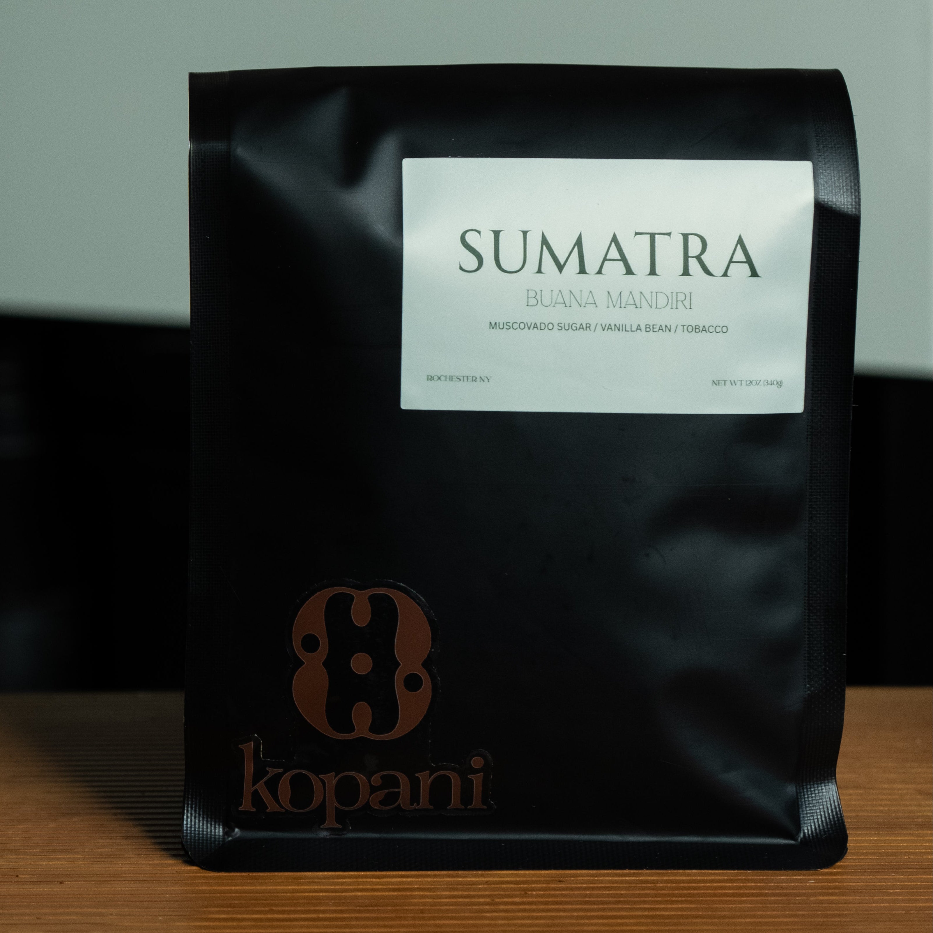 Black coffee bag labeled 'Sumatra' by Kopani on a wooden surface with a blurred background